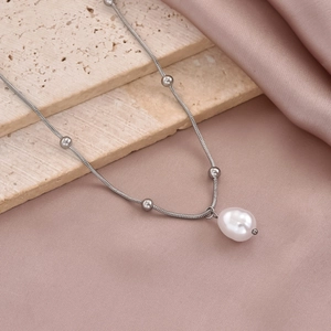 Detail shot of a silver snake chain necklace with round beads and a large pearl pendant