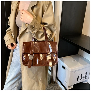 Close-up of brown glossy patent leather handbag with dual buckle flip-top design