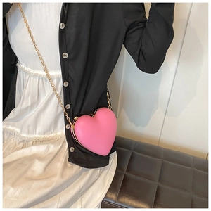 Model wearing a pink heart-shaped mini crossbody bag with a sleek gold chain strap