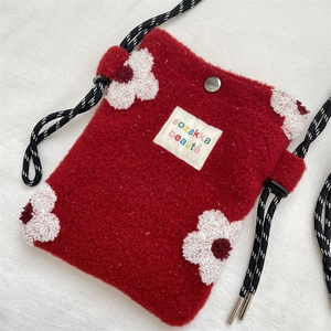 Close-up of red plush crossbody bag featuring floral embroidery and woven strap details