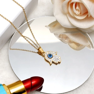 Close-up of golden Hamsa Hand necklace with blue Evil Eye charm on a mirror surface