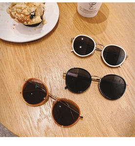 Tre paia di occhiali da sole rotondi vintage in bianco, nero e tartaruga su una scrivania