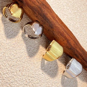 Polished gold and silver stainless steel open rings displayed on a rustic wood stand