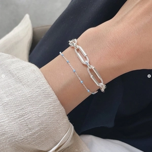 Detail of a 925 sterling silver paperclip and blue bead layered bracelet set on wrist
