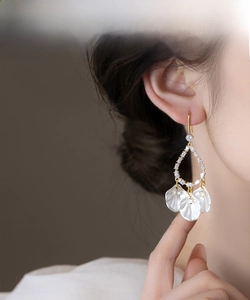 Gros plan de boucles d'oreilles dorées à glands avec coquillages blancs et cristaux