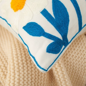 Cotton linen throw pillow with blue leaf embroidery and white flowers on a beige blanket