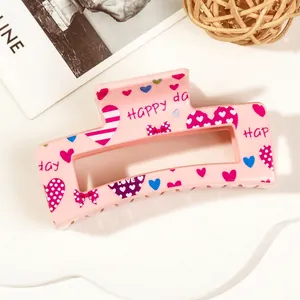 Close-up of pink heart-print hair claw clip with HAPPY DAY lettering and bow patterns