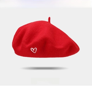 Detail of red wool beret showing delicate white heart embroidery and soft fabric texture