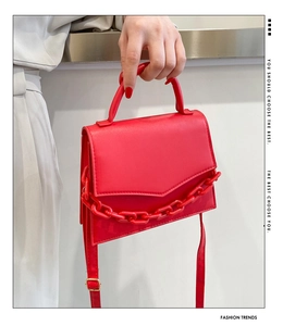 Detail of red crossbody bag with glossy finish, V-shaped stitching and thick resin chain