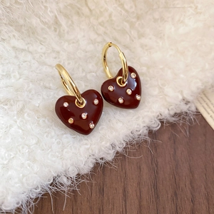 Close-up of gold heart earrings with burgundy enamel and diamonds on white plush