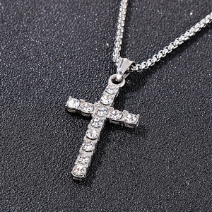 Vue macro d'un pendentif croix argenté orné de cristaux sur une chaîne en métal tissé