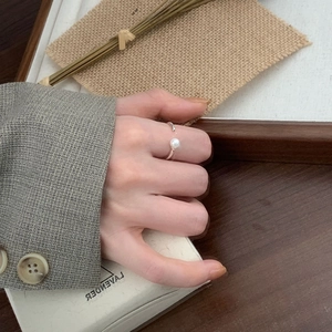 Detailed close-up of a minimalist silver pearl open ring worn on a finger
