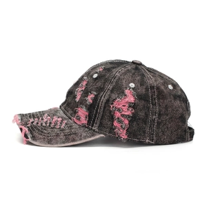 Side profile detail of distressed black denim baseball cap with pink frayed thread accents