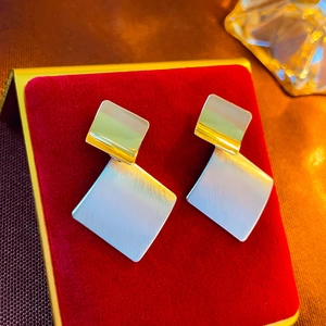 Detail of geometric mixed-metal earrings on red velvet with gold and silver finish