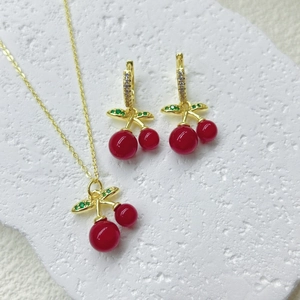 Makroansicht des Kirsch-Schmucksets mit roten Früchten und grünen Zirkonblättern auf Stein