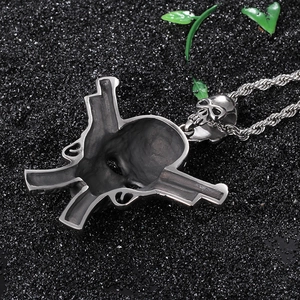 Macro shot of stainless steel skull pendant with double guns on black sand background