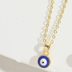 Macro view of golden evil eye necklace with blue enamel pendant on white background