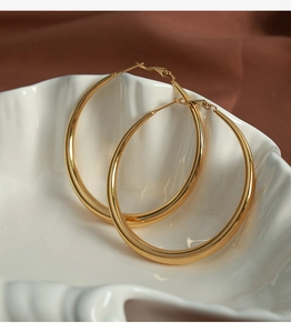 Détail de grandes boucles d'oreilles créoles dorées sur un plateau coquillage poli brillant