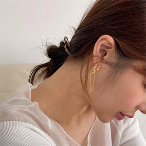 Macro detail of elegant gold knot drop earrings with minimalist hanging chain on ear