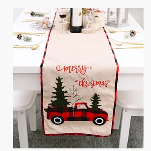 Close-up of Christmas table runner with red truck design and tartan border on festive table