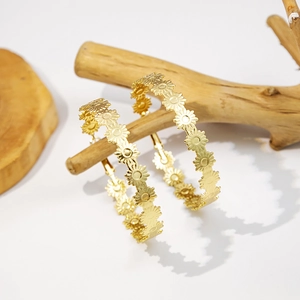 Detail shot of golden daisy flower hoop earrings hanging on a natural wooden display stand