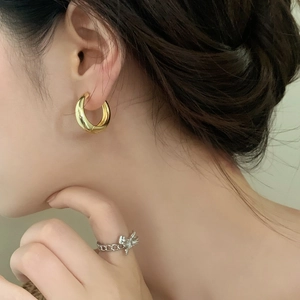 Close-up of minimalist gold hoop earrings and silver bow knot chain ring worn by a model