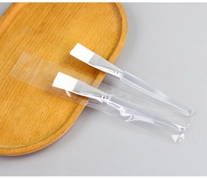 Macro shot of two facial mask brushes with white bristles on a wooden tray