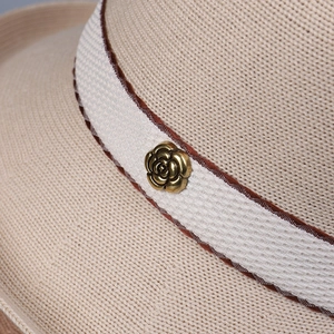 Detail of a beige knitted sun hat featuring a white fabric band with a bronze rose buckle
