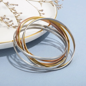 Close-up of stacked metallic bangles in gold, silver, and rose gold on a decorative tray