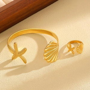 Detailed close-up of golden starfish and seashell open bangle and ring set on sand