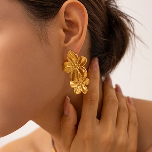 Close-up of elegant gold flower-shaped stainless steel earrings worn by a model
