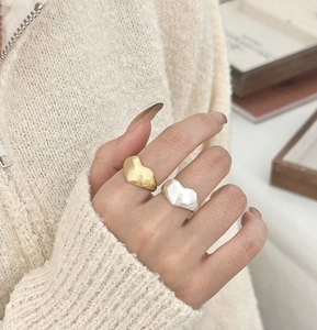 Close-up of gold and silver brushed heart rings worn by a model in a cozy setting