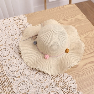 Detailed view of beige straw sun hat with rainbow pom-poms and wavy edge on wooden surface