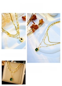 Macro shot of layered gold snake chain with heart charms and emerald square pendant