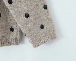 Dettaglio del polsino a coste su un maglione di maglia beige con motivi a pois neri