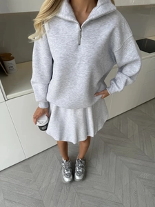 Flat lay of gray half-zip sweatshirt and pleated mini skirt set on wooden floor