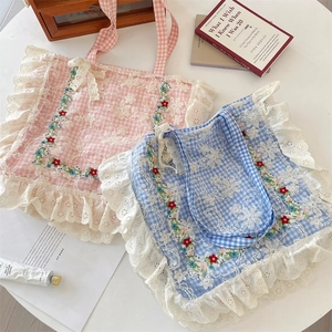 Detail of floral embroidery and lace trim on checkered canvas tote bags in a flat lay view