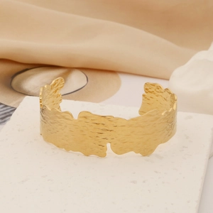 Close-up of golden wide cuff bracelet featuring irregular wavy edges and hammered texture