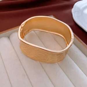 Polished golden hammered wide bangle featuring a hinged opening on velvet display