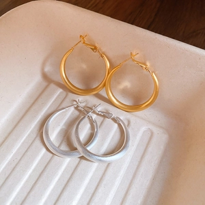 Detail of matte gold and silver large hoop earrings with textured finish on beige tray