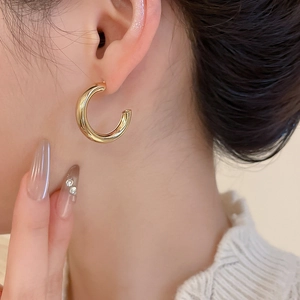 Detailed view of minimalist golden C-shaped hoop earrings worn by a model in soft lighting