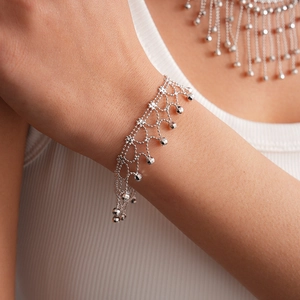 Close-up of minimalist silver tassel necklace and bracelet set on a white sweater