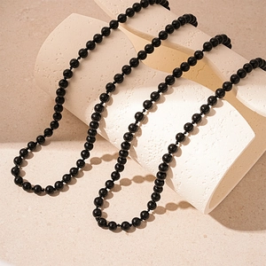 Detail of long polished black bead necklace on minimalist textured architectural props