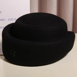 Detail of elegant black wool felt hat featuring a metallic M logo and rolled brim