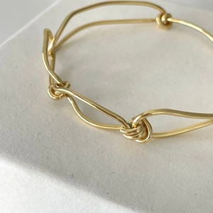 Macro shot of minimalist gold knot bracelet with woven metal detail and polished finish