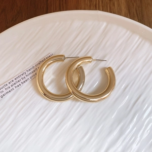 Top-down view of chunky golden C-shaped hoop earrings on white ceramic and wood surface