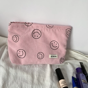 Pink corduroy makeup bag detail with minimalist smiley face and brand woven label