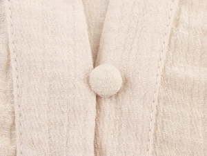 Detailed close-up of beige eyelet blouse featuring fabric-covered buttons and texture