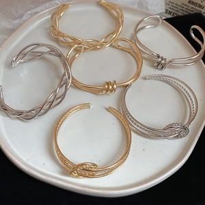 Close-up of gold and silver irregular twisted open bangles on a white ceramic plate