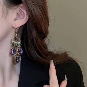 Close-up of bohemian leaf drop earrings with purple beads and bronze tassels on a model